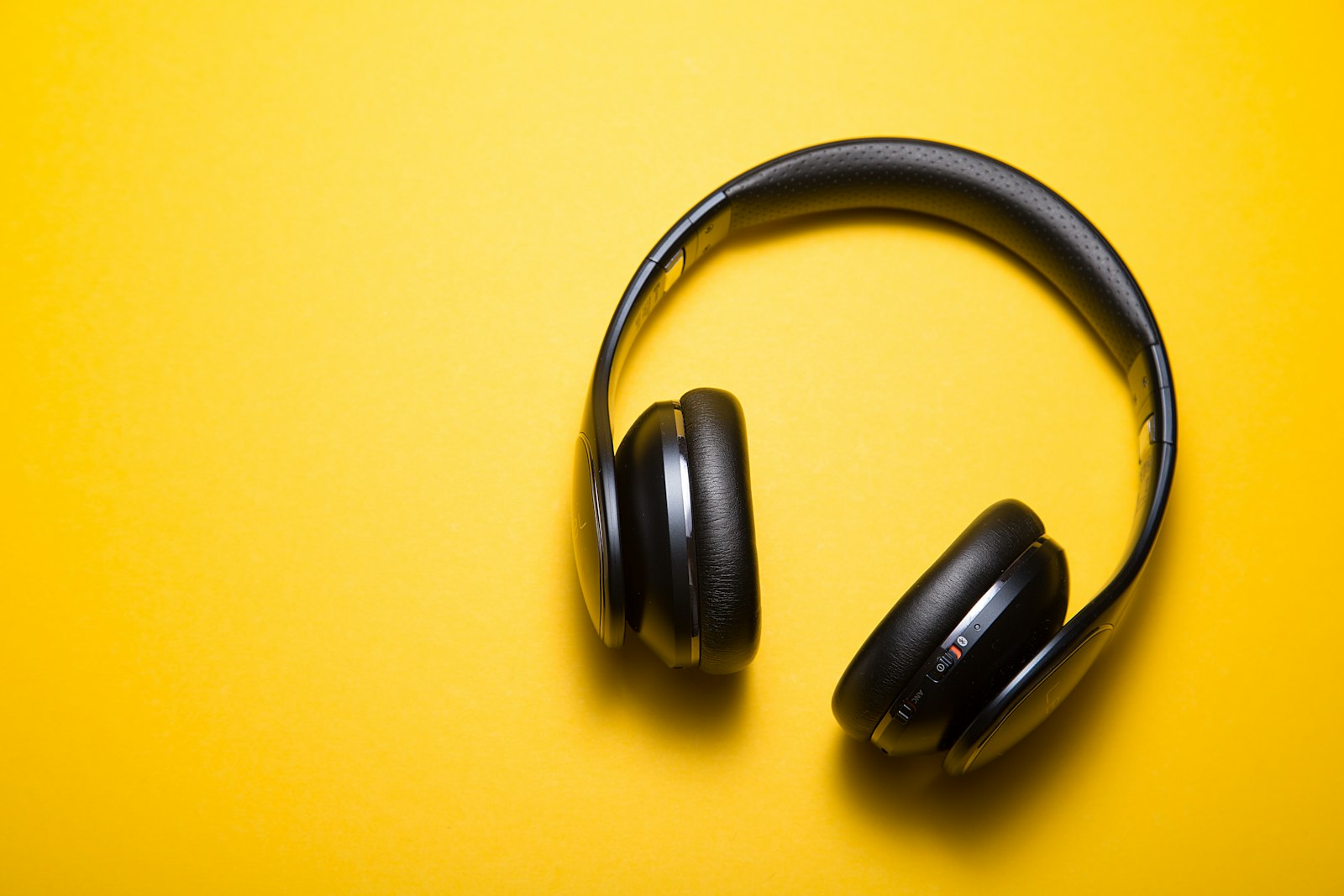 Black over-ear headphones with leather ear pads on a yellow background.
