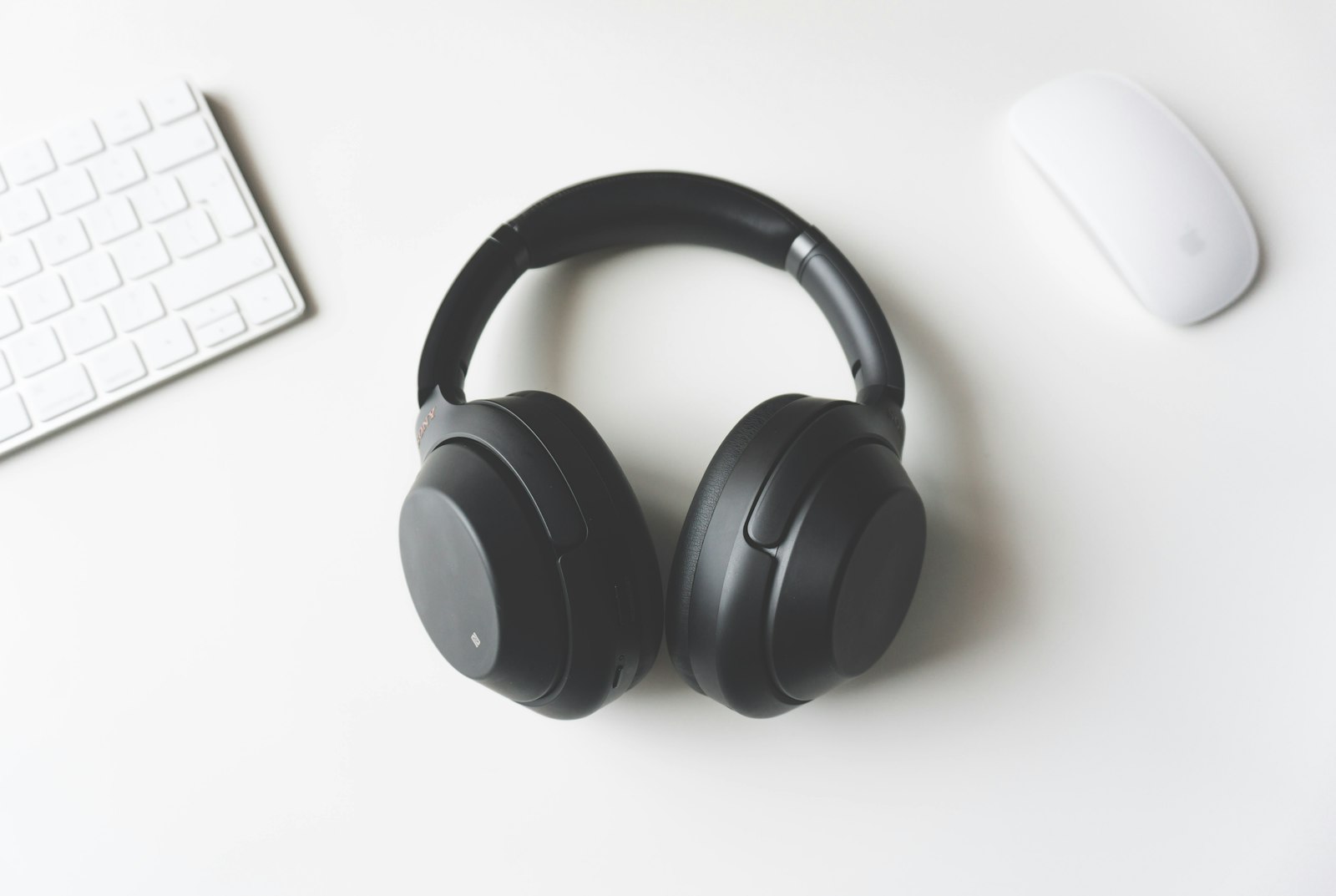 Black over-ear headphones on a white desk beside a keyboard and a mouse.